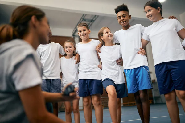 Low angle view of multi-ethnic group of elementary students having PE class with sports teacher at school gym.