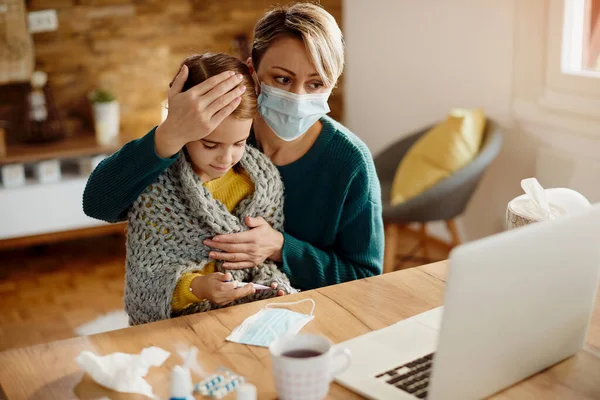 Single mother having video call with a doctor while her daughter is having high fever during coronavirus pandemic.