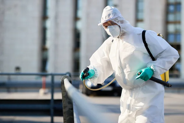 Male cleaner in protective suit disinfecting public area in the city due to coronavirus epidemic.