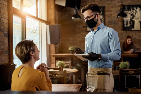 Happy Waiter Talking Female Customer While Wearing Protective Face Mask Immagine Stock