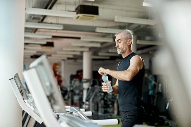 Olgun atletik adam koşu bandında koştuktan sonra su içer.