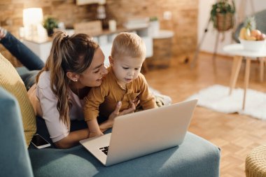 Cute little boy using computer with his mother while relaxing at home together. 