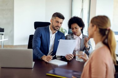 Members of human resource team talking while analyzing resume of a potential candidate during job interview in the office. 