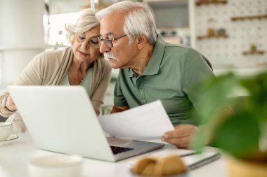Mature couple using laptop while analyzing their bills and paying them online at home. 