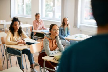 Teenage girl and her classmates listening teacher's lecture on a class in high school.