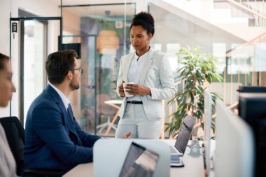 Black CEO having a briefing with her male colleague while he is working on computer at corporate office. 
