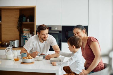 Happy parents and their small son having breakfast together at dining table at home. 