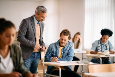 Mid adult student learning with teacher's assistance during a class at lecture hall.