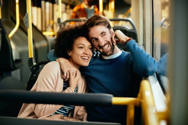 Happy couple embracing while commuting by bus and looking through the widow.