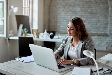 Happy businesswoman using laptop while working at her office desk. 
