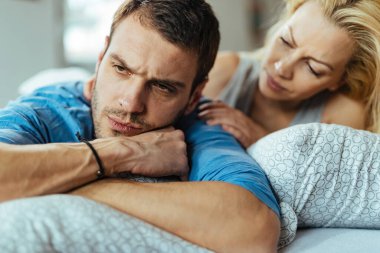 Displeased man ignoring his girlfriend while lying down in bed after the argument. 