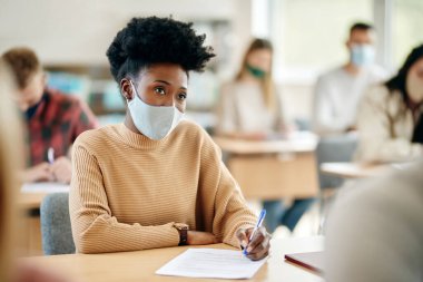 African American female student wearing face mask while attending a class at the university during coronavirus pandemic. 