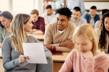 Happy university friends communicating while attending lecture in the classroom. Focus is on happy black student. 