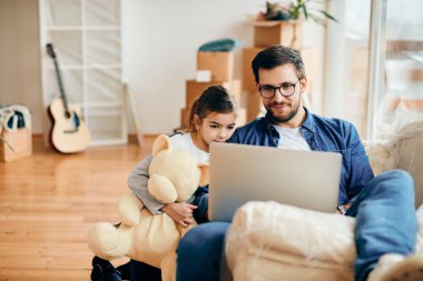 Happy father with daughter surfing the net on a computer after moving into a new home. 