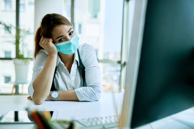 Young businesswoman wearing face mask and thinking of something while working alone in the office. 