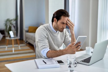 Distraught businessman reading problematic e-mail on touchpad while working at home. 