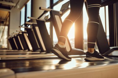 Close-up of athletic woman warming up and walking on treadmill in a gym. Copy space.