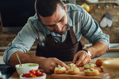 Genç adam mutfakta avokado bruschetta hazırlıyor..
