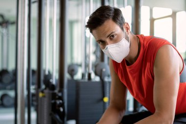 Male athlete wearing protective face mask in health club and looking at camera. 