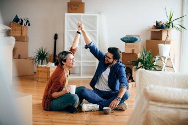 Happy couple holding hands and having fun while sitting on the floor at their new home.