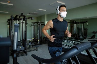 Athletic man wearing face mask while running on running track in health club during coronavirus epidemic. 