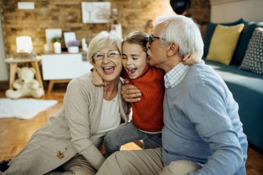 Cheerful little girl having fun and embracing her grandparents at home. 