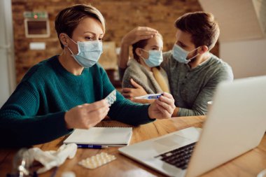 Woman with face mask using computer and having consultations with doctor about daughter's medicine due to COVID-19 pandemic. 