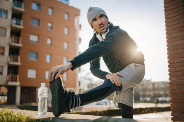Low angle view of male athlete warming up and stretching his leg while preparing for sports training outdoors. 