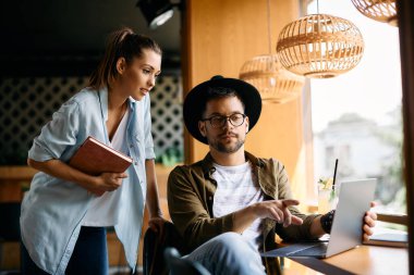 Young student and his female friend using laptop while studying together in a cafe. 