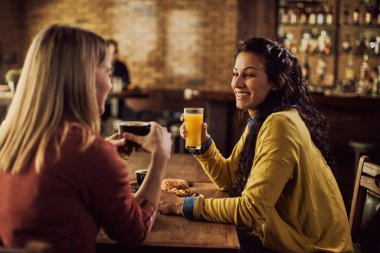 Young happy woman communicating with her female friend while drinking juice during lunch in a pub. 