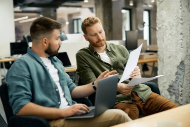 Male entrepreneurs cooperating while analyzing business reports in the office. 