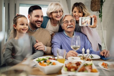 Happy multi-generation family having fun while taking selfie during lunch in dining room. 