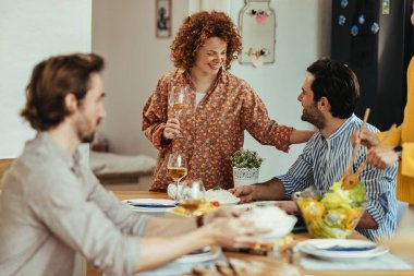 Young smiling couple talking to each other during lunch time with their friends in dining room. 