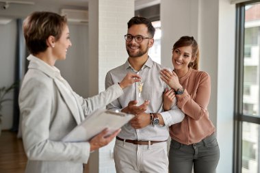 Young happy couple receiving new house keys from real estate agent. 
