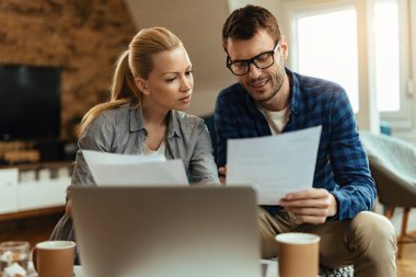 Smiling man and his wife analyzing their financial bills and paying them online at home. 