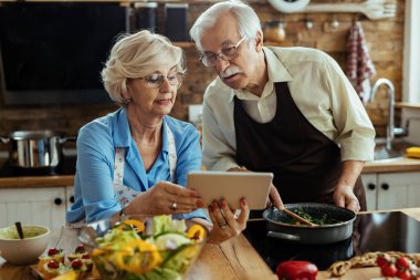 Mature couple reading recipe on digital tablet while preparing lunch in the kitchen. 