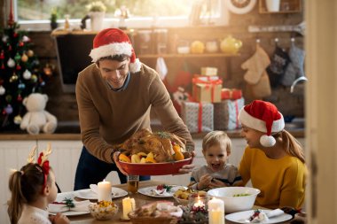Happy parents and their small kids having stuffed turkey for Christmas lunch at home. 