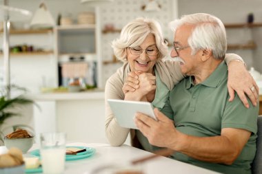 Happy mature couple holding hands while using touchpad at home. 
