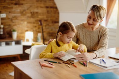 Happy mother teaching her daughter to read during homeschooling. 