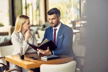 Business couple choosing order form a menu and communicating at the table in a restaurant.