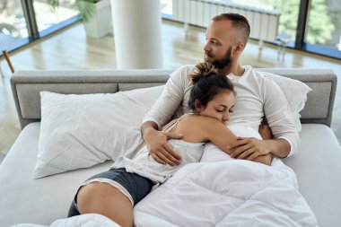 High angle view of young couple in love embracing while lying down on bed. 