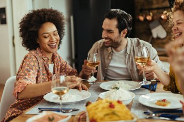 Group of happy friends having fun while eating together at dining table. Focus is on African American woman. 