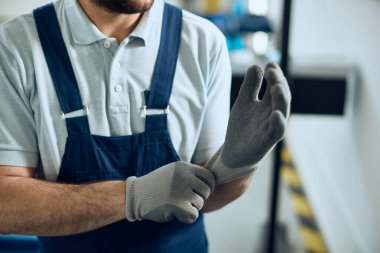 Close-up of auto repairman using protective gloves while working at workshop. 