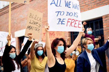 Large group of protesters wearing protective face mask while walking through city street and supporting Black Lives Matter movement. 