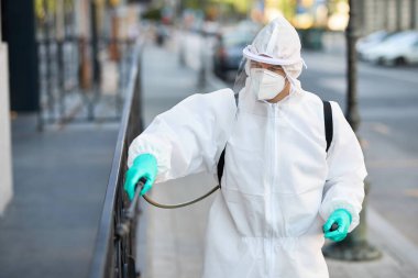 Disinfection worker in hazmat suit spraying city streets during COVID-19 pandemic. 