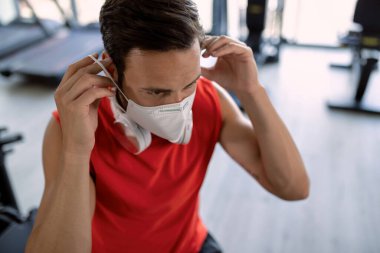 Athletic man using protective face mask while exercising in a gym during COVID-19 epidemic.