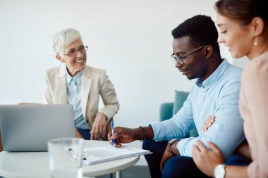 Happy signing an agreement while having a meeting with their insurance agent. Focus is on black man signing paperwork. 