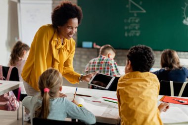 Happy African American teacher and school kids using touchpad on a class at the school. 