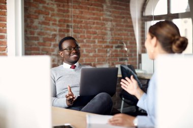 Happy coworkers communicating on a break in the office. Focus is on African American businessman with laptop. 
