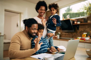 Happy black parents with kids using computer ad greeting someone during a video call. 